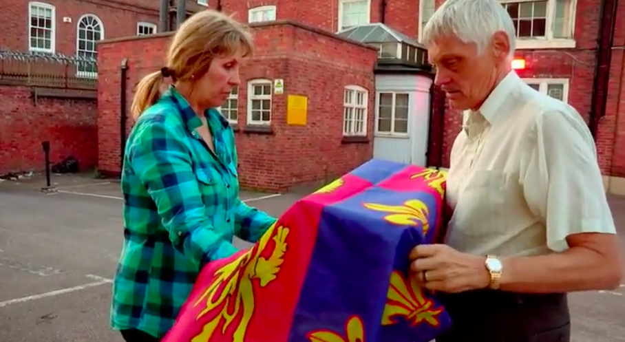 Philippa and John placing Richard's colours over his remains.